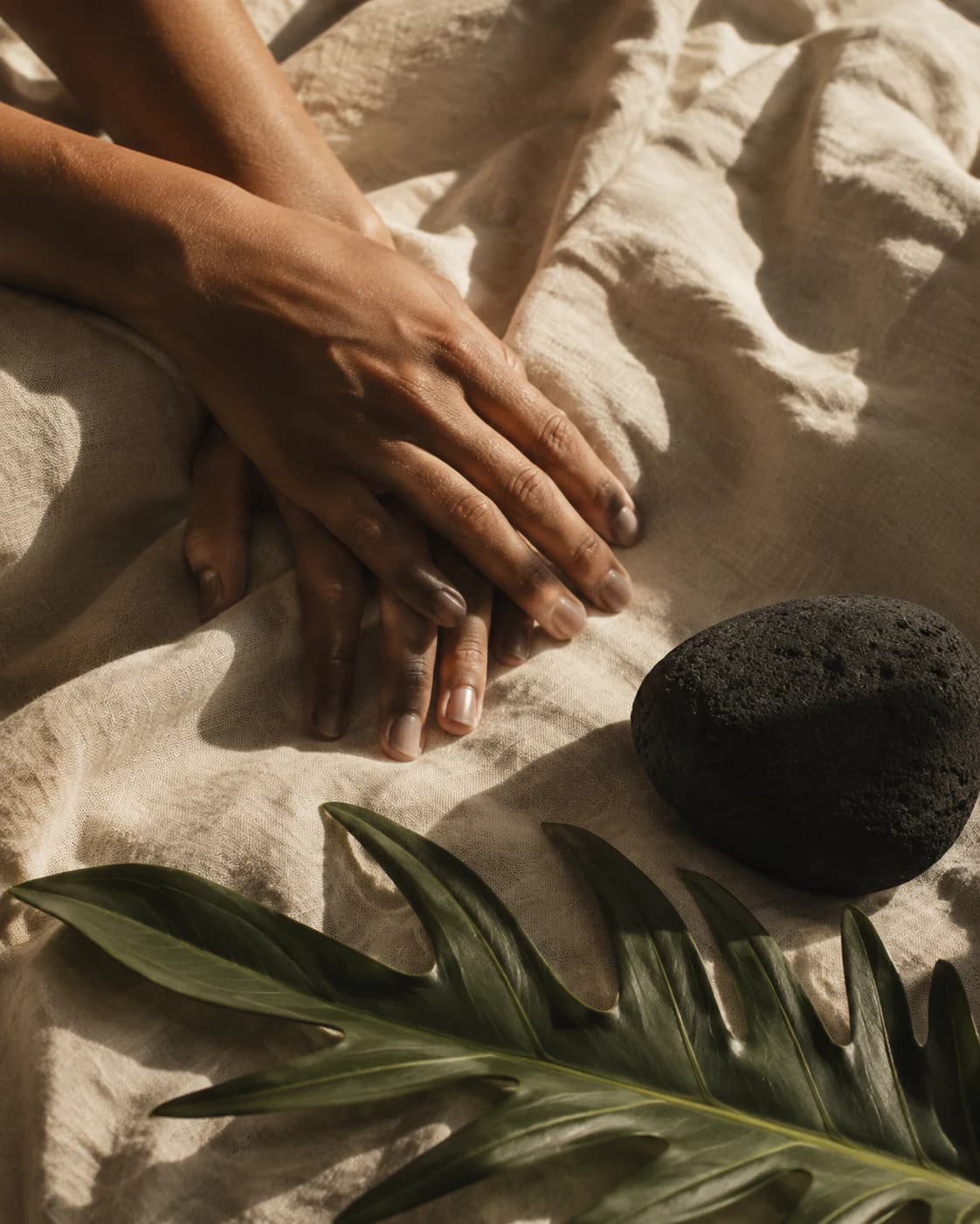 Mains au repos sur un linge naturel, près d’une pierre volcanique et d’une feuille tropicale